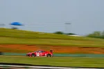 Red race car number 93 speeding on a green racetrack with blurred background showing motion.