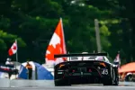 Rear view of black race car number 45 on track with Canadian flags and spectators in the background