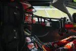 Race car driver wearing red helmet and gloves seated inside a race car cockpit ready to drive.