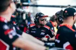 Race team members wearing headsets and branded uniforms communicating in the pit area during an event