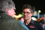 Man with glasses smiling and talking to another person at an outdoor event during nighttime.