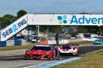Red Acura race car leading prototype and blue race cars on Sebring race track under bridge banner on sunny day