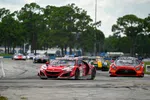 Red and orange race cars speeding on a track during a professional motorsport event with trees in the background