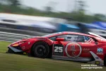 Red Lamborghini race car number 25 speeding on racetrack with sponsor logos and American flag decal.