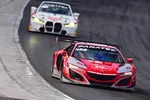 Red and white Acura NSX GT3 race car leading a white BMW M4 GT3 on a curved racetrack during a motorsport event.