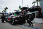 Pit crew changing tire on black and red race car number 45 during motorsport event in busy pit lane