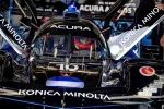 Race car driver in black Acura Konica Minolta car with open doors preparing for the race in the garage.