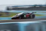 Black and red race car number 45 speeding on a curved racetrack with blue barriers in the background