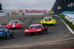 Four colorful race cars competing on a curved race track under cloudy skies near a Sahlen's billboard.