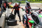 Pit crew changing tires on a race car during a fast-paced motorsport pit stop at a sunny racetrack.