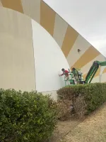 Worker on lift painting a large white semicircle on a building with yellow and beige sunburst design.