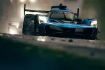 Blue Acura race car with headlights on racing on wet track during rainy conditions.