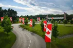 Curved road lined with Canadian flags and trees under a partly cloudy sky in a green landscape.