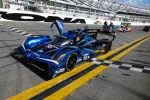 Blue Acura race car number 10 with open cockpit on Daytona racetrack pit lane under clear sky.