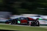 Black and red race car number 45 with green accents speeding on racetrack with blurred background.