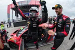 Race car driver celebrating victory beside red GT3 car with team member at motorsport event podium area.