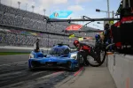 Blue Acura prototype race car refueling during daylight pit stop at a professional racing track with pit crew member.