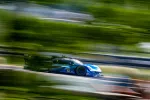Blue and black race car speeding on a track with motion blur and green background during daytime.