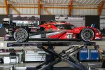 Red and black race car number 40 elevated on a hydraulic lift inside a garage with tools and equipment.