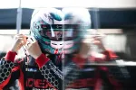 Race car driver in helmet and racing suit adjusting gear with motion blur reflection in background.