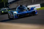 Blue Acura prototype race car speeding on track with a green car in the background during a race.