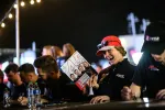 Cheerful woman in red cap holding a racing magazine at a nighttime motorsport autograph event