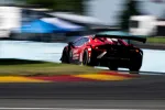 Red racecar speeding on track with motion blur and colorful curbs under a bright sky.