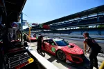 Red race car number 93 in the pit stop with crew members preparing during a sunny day at the racetrack.