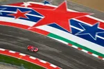 Aerial view of a red race car speeding on a curved track decorated with large red, white, and blue stars and stripes.