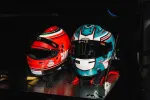 Two racing helmets with visors on a metallic surface, one red and the other white and teal with racing decals.