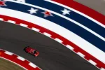 Red race car speeding on curved race track with red white and blue patriotic star pattern barriers.