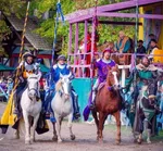 Four knights in colorful medieval armor on horses holding lances at a Renaissance fair jousting event.