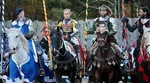 Four medieval knights in armor on decorated horses holding lances during a jousting event outdoors.