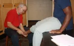 Doctor examining patient's ankle in a medical office with stethoscope and paperwork on the desk