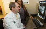 Doctor and assistant reviewing medical scans on computer monitor in clinical office setting