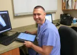 Male healthcare professional in blue scrubs reviewing digital medical records with X-ray image on computer screen