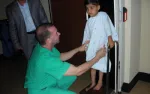 Doctor in green scrubs assisting young boy in hospital gown on a scale in medical facility