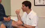 Doctor examining patient's knee and discussing treatment in a medical office setting.