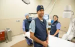 Medical team in protective gear standing in a hospital operating room with advanced imaging equipment.