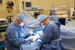 Surgeons in blue scrubs performing surgery in a modern operating room with medical equipment.