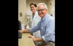 Male patient and female doctor at a medical office using a computer, smiling towards the camera.