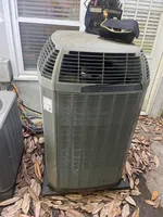 AC Repair in Peachtree Corners by The Air Company of GA.  Outdoor air conditioning unit with tool bags on top and dry leaves scattered around on the ground.