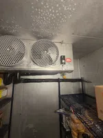 Commercial Refrigeration Repair in Atlanta by The Air Company of GA. Commercial walk-in cooler interior with cooling fans, condensation on ceiling, metal shelves, and stored food items.