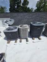 Smyrna HVAC Diagnostic Repair and Replacement by The Air Company of GA.  Three rooftop air conditioning units on wooden blocks with a satellite dish and shingled roof background under a sunny sky.