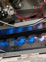 Blue flame burners operating inside a furnace with visible wires and a component test instruction sticker.