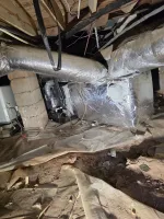 Crawl space with insulated HVAC ducts, exposed dirt floor, and wooden beams overhead in a basement area.