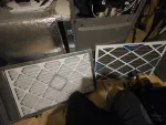 Two HVAC air filters next to an open furnace with tools on a wooden floor during maintenance.