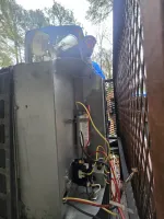 AC-Capacitor-Replacement-Atlanta-30307-HVAC-Repair-The-Air-Company-of-GA Air conditioning unit internal components and wiring with a technician in the background near a metal fence.