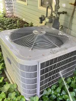 Ac Repair and Maintenance in Smyrna 30080 by The Air Company of GA.   Outdoor air conditioning unit surrounded by green ivy plants next to house siding and piping.