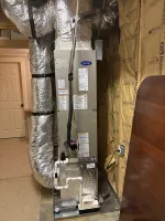 Carrier HVAC unit with insulated ductwork installed in an unfinished room with exposed insulation and pipes.
